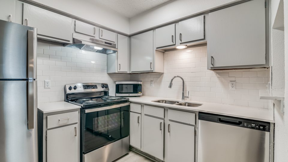a kitchen with stainless steel appliances and white cabinets at The Falltree Apartments